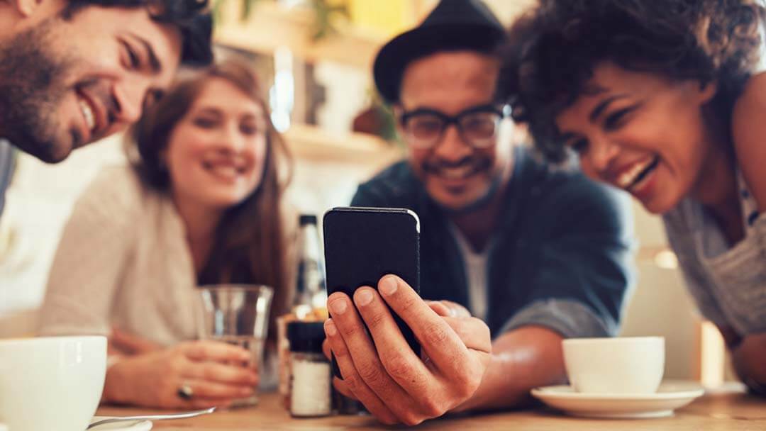 Group of friends smiling and looking at a smartphone, symbolizing an online marketing agency fostering engagement.