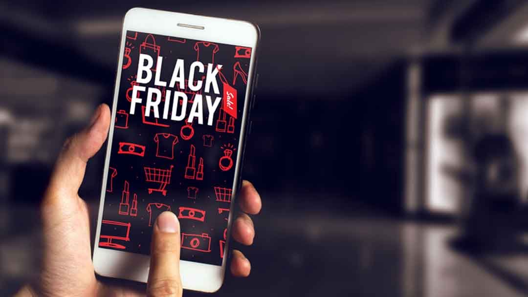 Close-up of a hand holding a smartphone displaying Black Friday sale graphics with red icons in a dimly lit background.