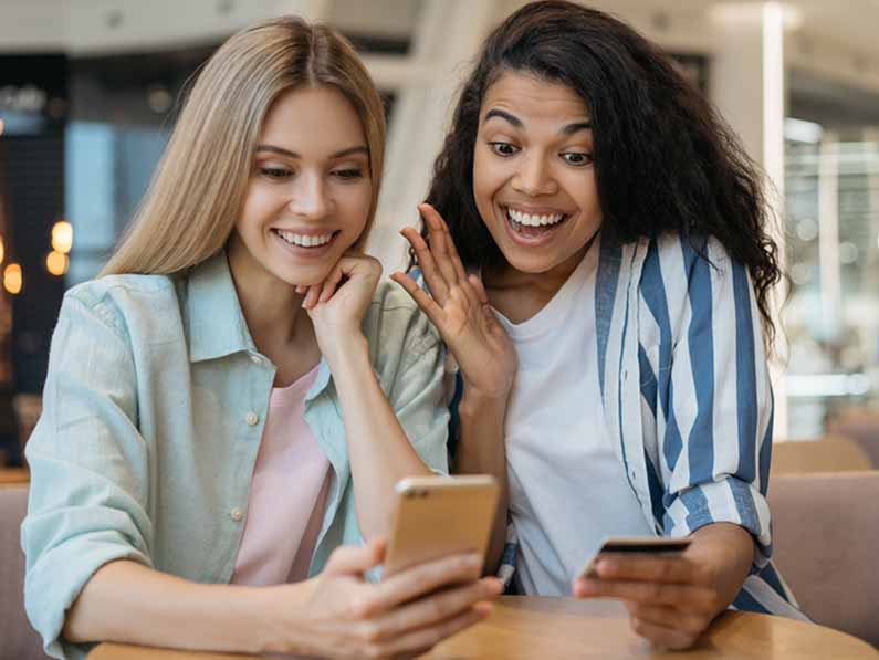 Branding agency helping clients boost conversions in Roseville Sacramento Two women smiling at phone with credit card, representing branding agency success, client conversions, and digital strategy.