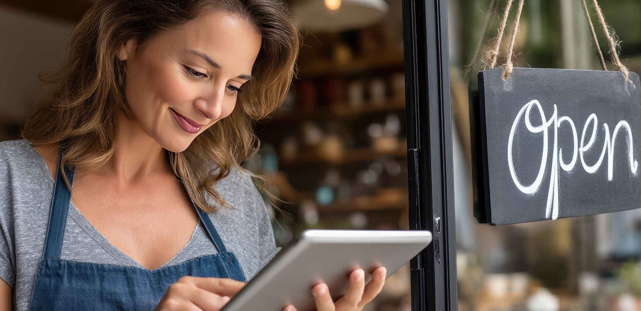 Smiling, satisfied female entrepreneur uses tablet outside her shop, representing SWOT analysis and market research services in Sacramento Roseville